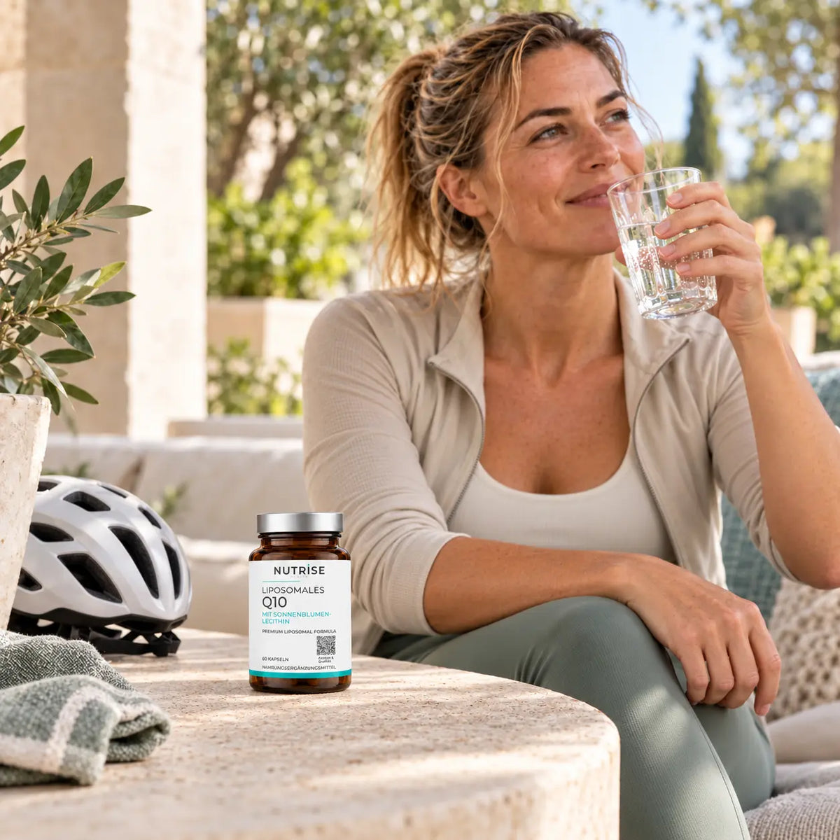 Nutrise Q10 im Alltag: aktive Frau mit Fahrradhelm, Wasser und dem Produkt
